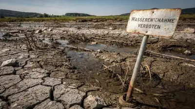 Vertrocknetes Flussbett mit aufgerissenem Schlamm und verrostetem Schild "Wasserentnahme verboten" in karger Landschaft